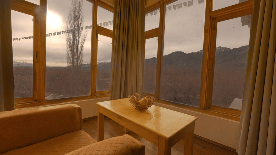 A view from a comfortable indoor seating area looking out through large windows towards the mountains at Indus Serenity Retreat.