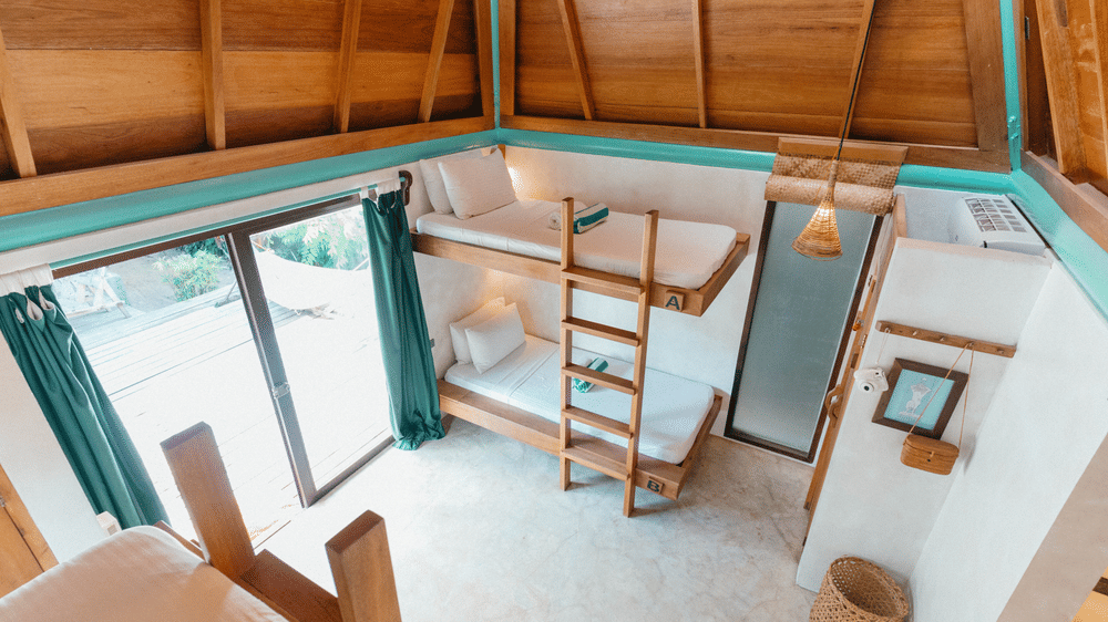 Surf Shack interior at Bravo Beach Resort Siargao with 2 bunk beds, a wooden ladder, a timber A-frame ceiling, and a glass door opening to the sun deck