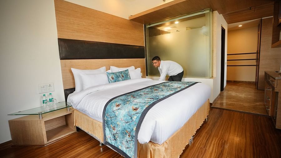 Bedroom with a neatly made bed, wooden floor, and a partially open wardrobe, creating a cosy space - VITS Gurugram