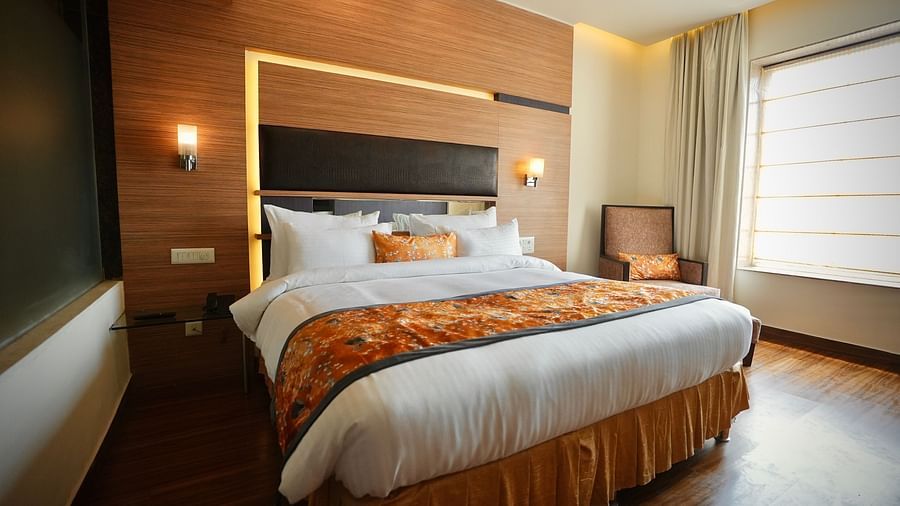 A bedroom featuring a bed with patterned bedding, a window with curtains, and a wooden wall panel - VITS Gurugram