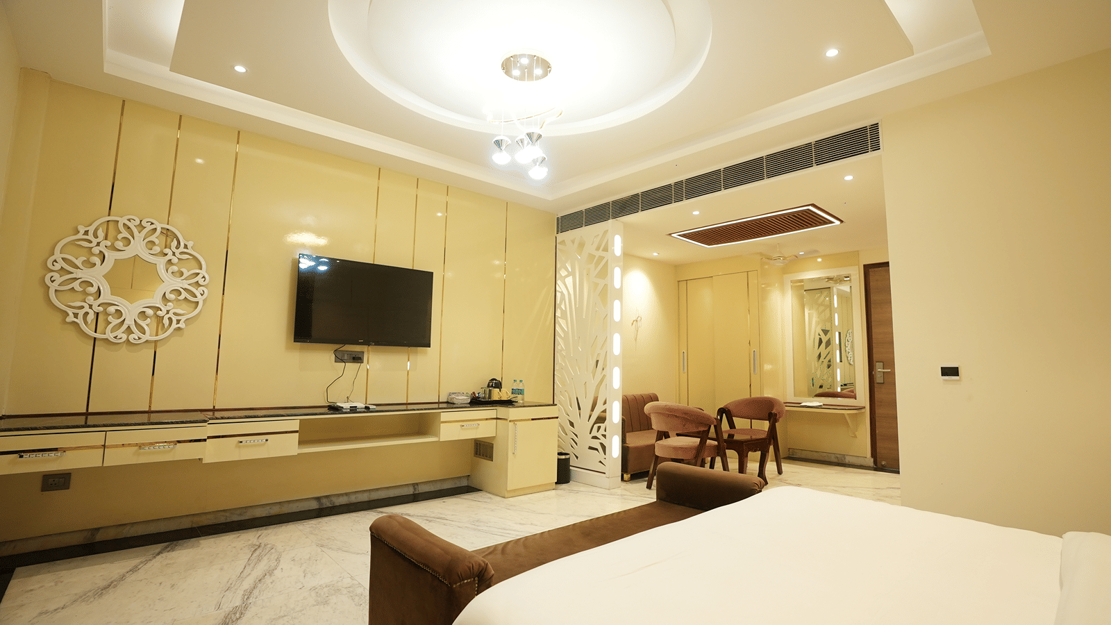 Modern hotel suite with a wall-mounted television, long wooden console table, and crisp white bed linens.