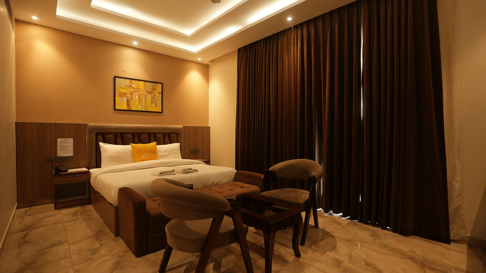 Wide perspective of a hotel bedroom displaying elegant recessed ceiling lighting and a small dining setup.