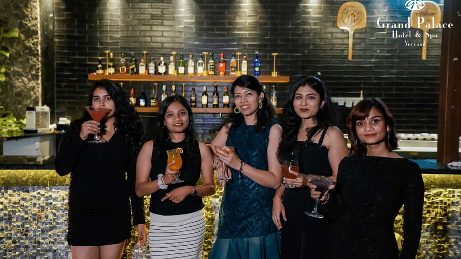 Group of ladies at the bar in Grand Palace, Yercaud holding glasses near the counter with illuminated bottle rack and wall lights.