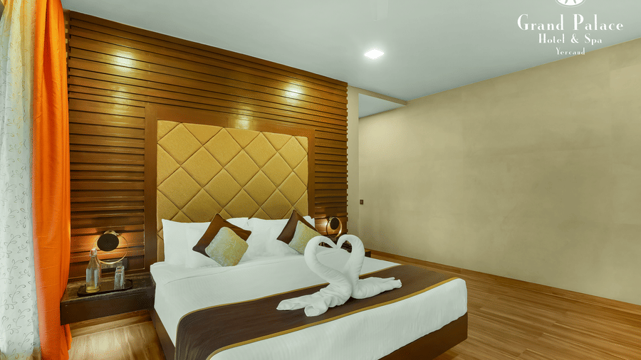Artist Suite at Grand Palace, Yercaud with double bed, bedside tables, headboard, lighting and curtains, showing modern indoor accommodation.