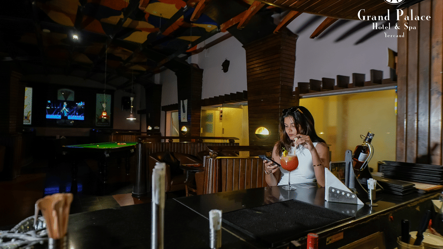 A lady at Cloud-9 Bar, Grand Palace, Yercaud preparing drinks near the bar counter with seating booths and billiards table.