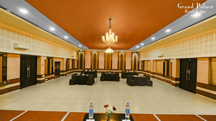 Banquet hall at Grand Palace, Yercaud with round tables, dining chairs, stage, spotlights, golden ceiling feature, and audio equipment set up for function.