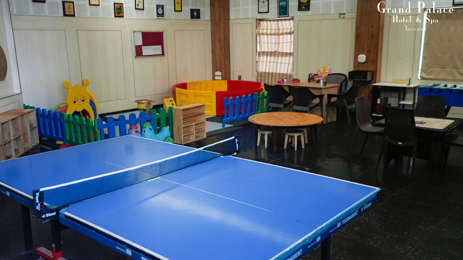 Table tennis setup in play zone at Grand Palace, Yercaud, with blue ping pong table, chairs, colourful barriers, and decorated walls in recreation room.