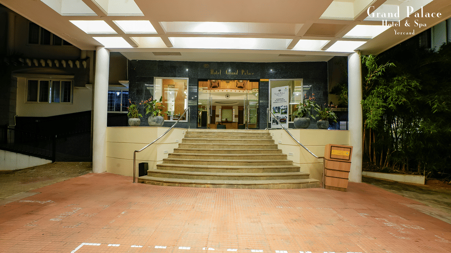 Main entrance with steps and covered area at Grand Palace, Yercaud, showing driveway, illuminated entrance, and surroundings.