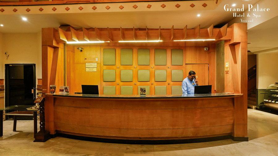 Reception desk at Grand Palace, Yercaud, with check-in counter, staff, service desk, and large wall display.