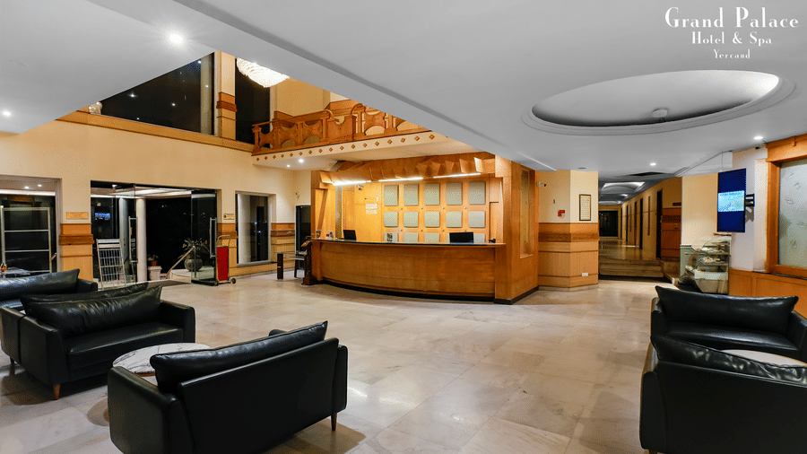 Lounge at Grand Palace, Yercaud, with multiple sofas, tables, visible reception, and open area for guest relaxation.