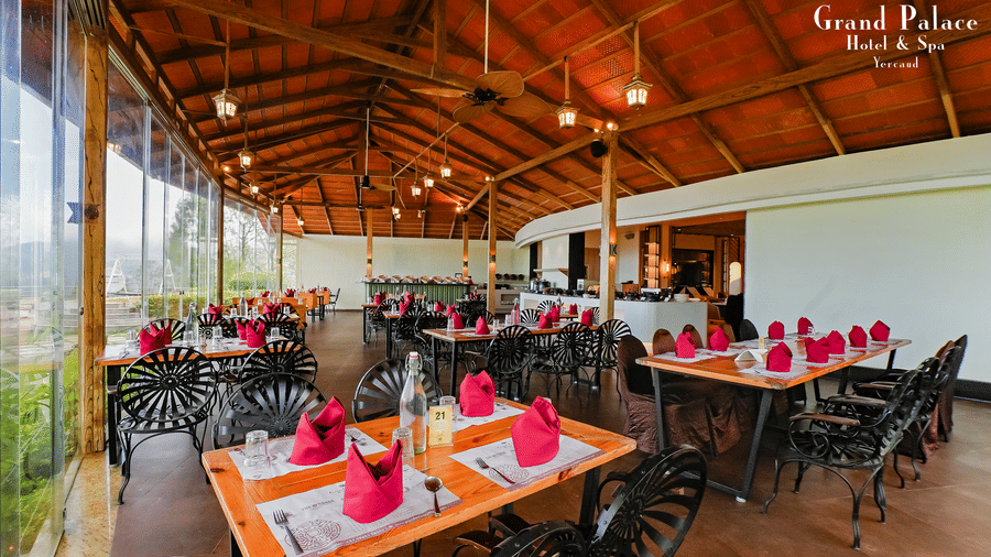 Dining area at Grand Palace, Yercaud showing tables set with red napkins, chairs, and open roof structure.