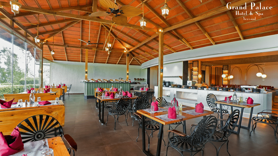 Dining area at Grand Palace, Yercaud with tables arranged under a wooden roof structure with open glass windows.