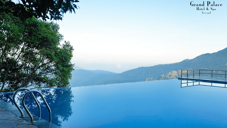 Infinity pool at Grand Palace, Yercaud with boundary railing, mountain valley view, water surface, trees, open sky, and platform ledge.