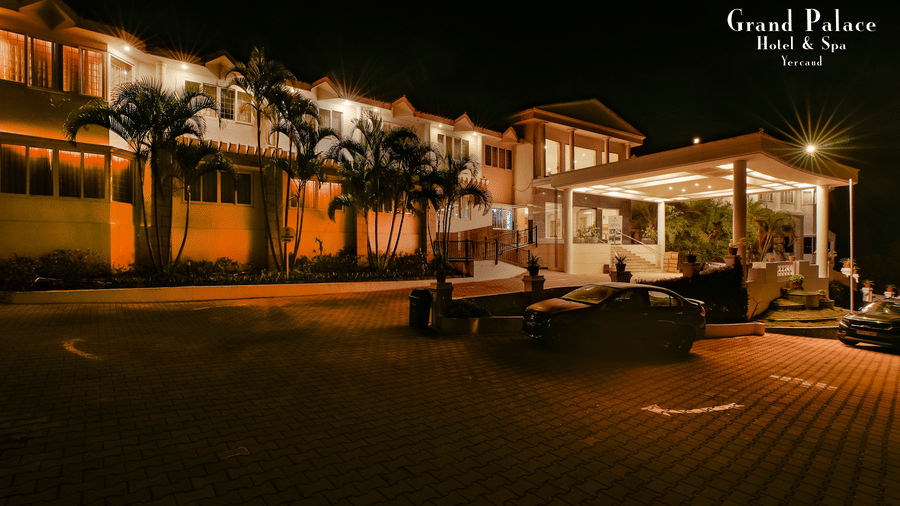 Exterior shot at night at Grand Palace, Yercaud, capturing entrance steps, main building, drive, and outdoor seating area.