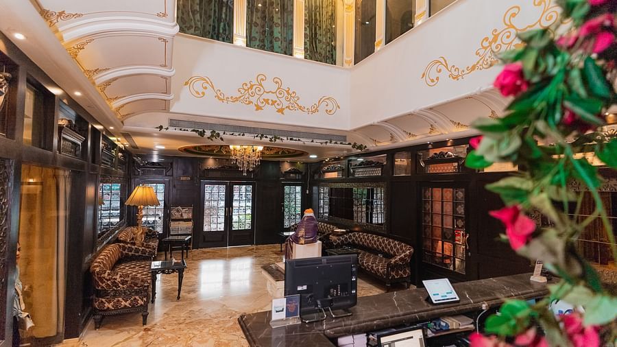 Hotel Ashok Nagpur featuring a wooden check-in counter with a computer and other equipment, a blurred figure in the background, and a floral arrangement on the side.