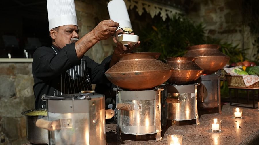 A chef carefully prepares a buffet, stirring dishes in traditional copper vessels - Khas Bagh, Jaipur.