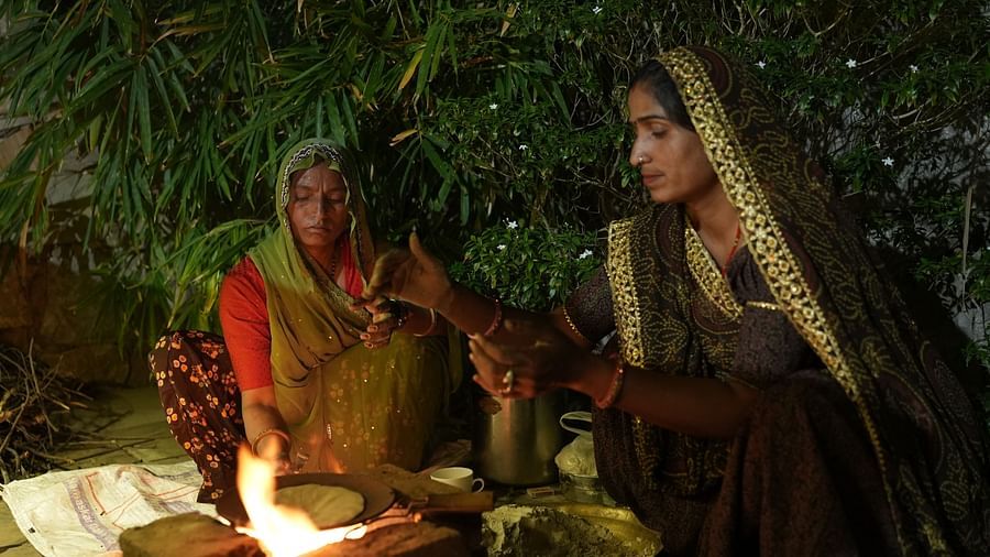 Village women dressed in traditional attire cooking over a fire under a leafy canopy - Khas Bagh, Jaipur.