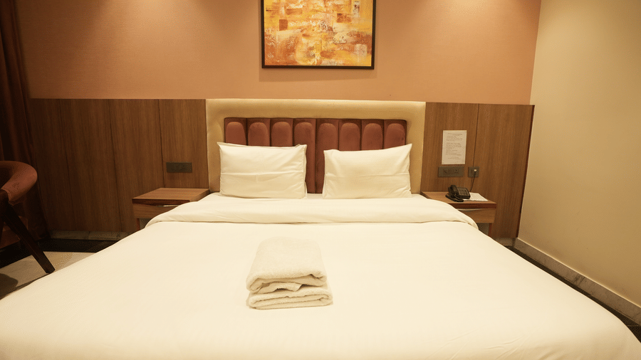 A centred perspective of a large hotel bed with a buttoned leather headboard and abstract artwork above.