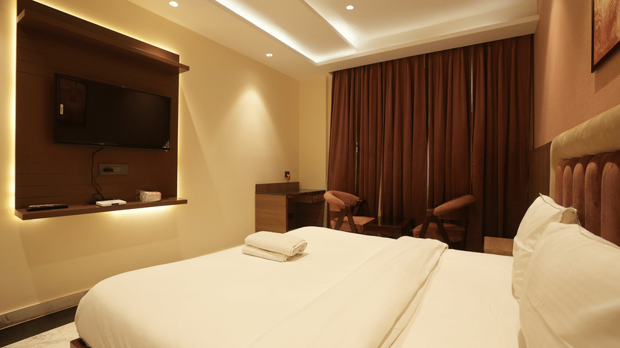 Comfortable hotel bed positioned across from a wall-mounted television panel under warm recessed lighting.