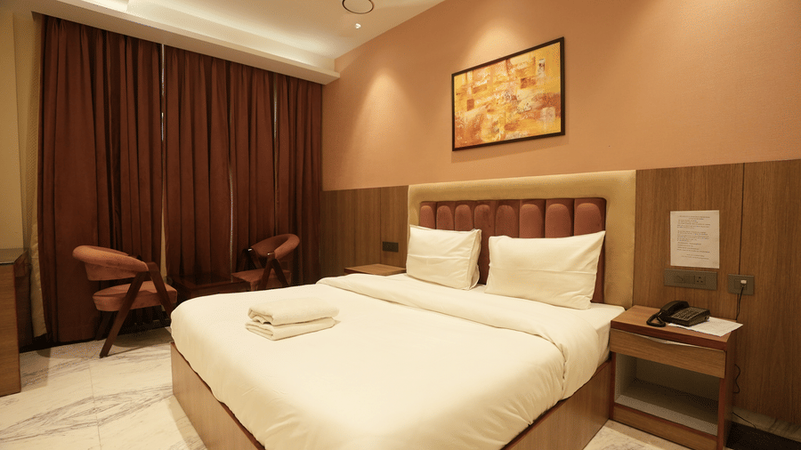 A stylish hotel bedroom featuring a neatly made double bed with white linen next to a dark wood bedside cabinet.