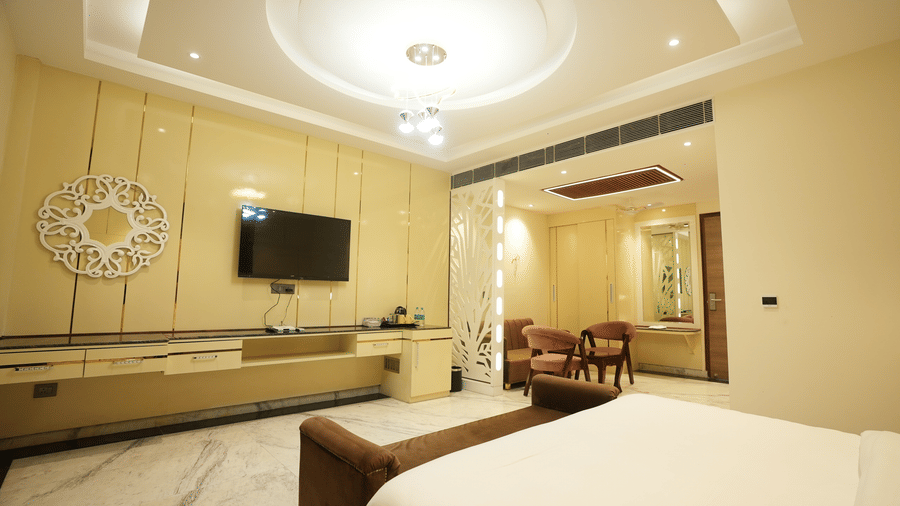 Modern hotel suite with a wall-mounted television, long wooden console table, and crisp white bed linens.
