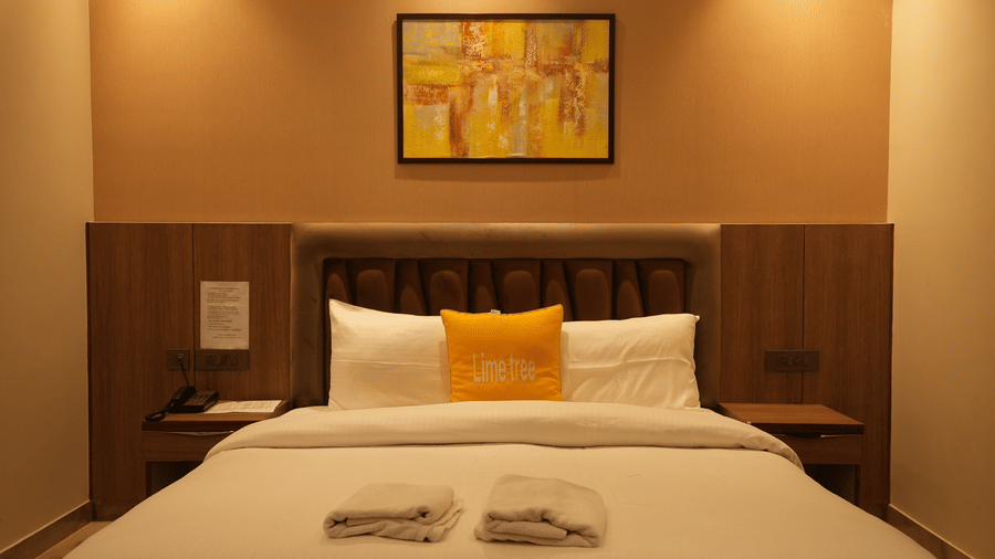 A centred shot of a neatly dressed double bed with a wooden headboard and a colourful abstract painting above.