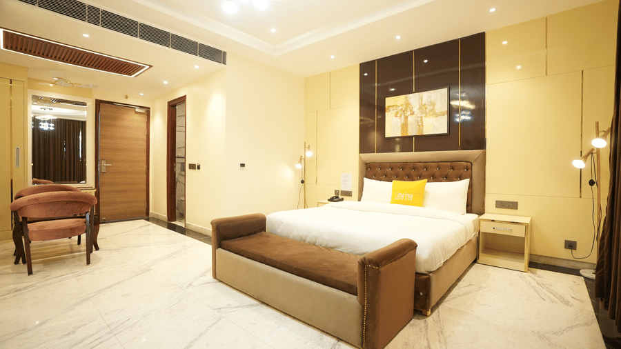 Large hotel bedroom showing a king-size bed with a brown leather bench and a classic armchair in the corner.