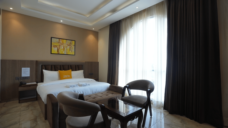 Premium hotel suite with a king-size bed, dark full-length curtains, and two comfortable armchairs.