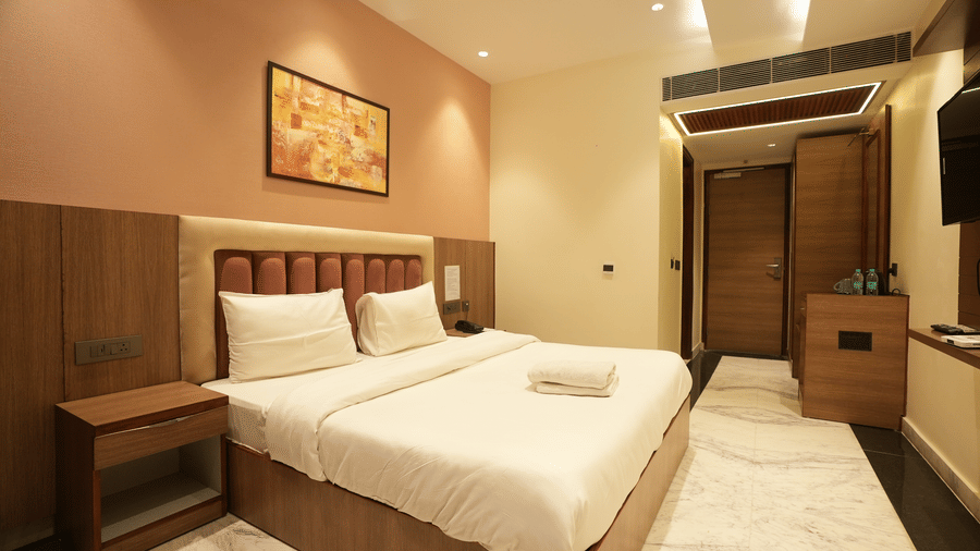 Wide view from the entrance of a contemporary hotel room displaying a dressed bed and marble flooring.
