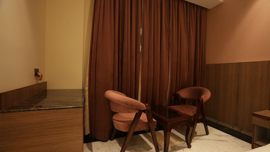 A cosy in-room seating space featuring two pink accent chairs and a small coffee table near heavy drapes.