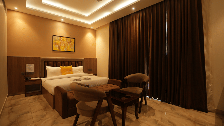 Wide perspective of a hotel bedroom displaying elegant recessed ceiling lighting and a small dining setup.