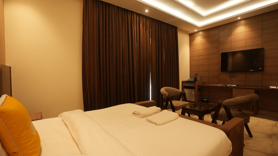 Warmly lit hotel room featuring a large double bed, yellow cushions, and a wall-mounted television screen.