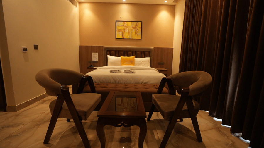 Symmetry shot of a hotel room lounge area with wooden chairs, coffee table, and a bed in the background.