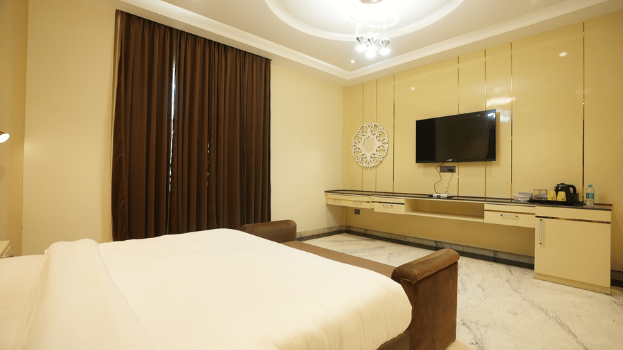 Elegant hotel bedroom setting featuring a dressed bed facing a wooden media console with a flat-screen TV.