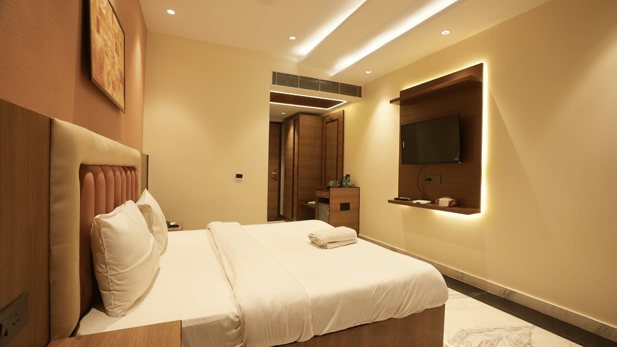 Neatly arranged double bed with white pillows next to a wooden wall fixture and warm, ambient lighting.