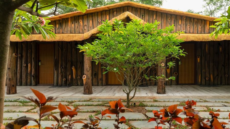 A wooden building with a thatched roof, surrounded by trees and plants, suggests a natural or rustic setting | Standard Room | RD's Nature Retreat, Bangalore
