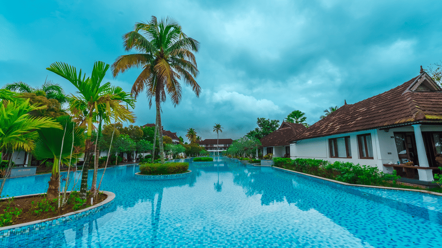 Rhythm Kumarakom features a tranquil infinity pool overlooking lush gardens and elegant villas beneath cloudy skies.