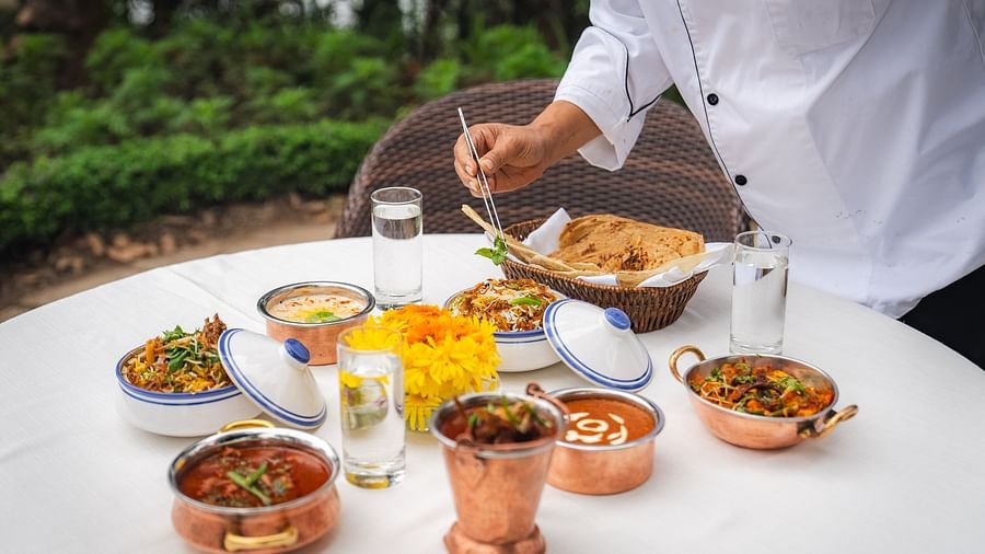 Chef serving an exquisite Indian meal in copper utensils at an outdoor dining setup at The Claridges Nabha Residence