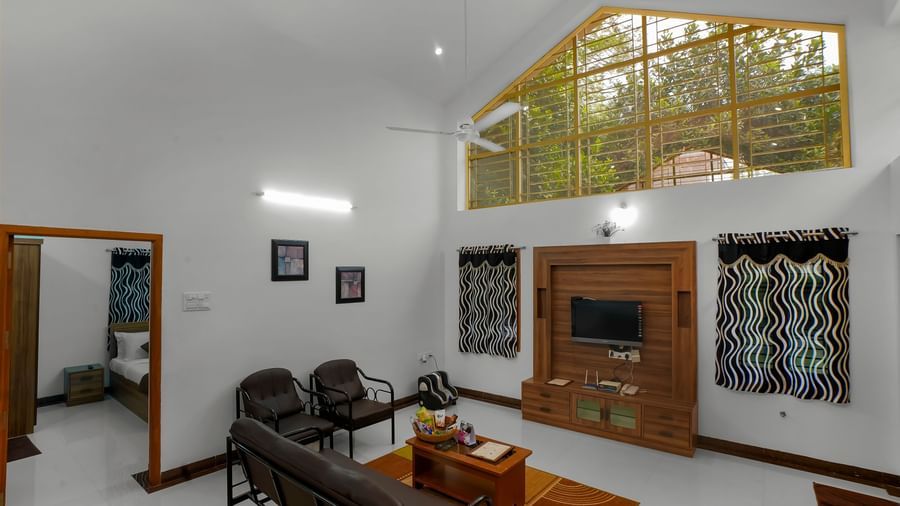 Living room with a sofa and wall-mounted television with a wooden cupboard at WOW Bungalow, Yercaud.