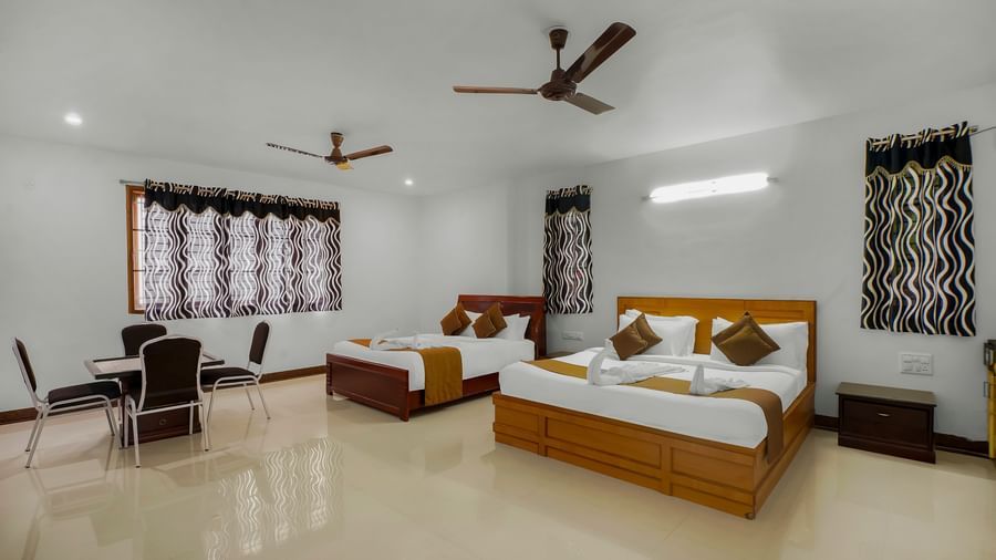 Spacious bedroom with two beds, a table with chairs placed around it and windows with a curtain at WOW Bungalow, Yercaud.