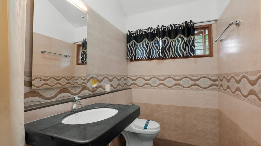 Spacious washroom with a washbasin, a wall-mounted mirror and a western toilet at WOW Bungalow, Yercaud.