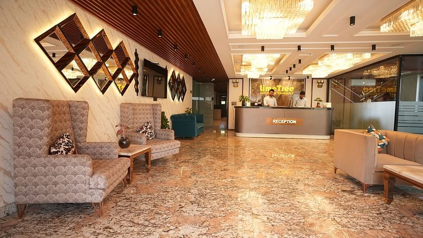 An image of a reception lobby with sofa sets and sofa chairs, and there is  a reservation desk where two receptionist are standing - Lime Tree Hotels & Service Apartment Private Limited