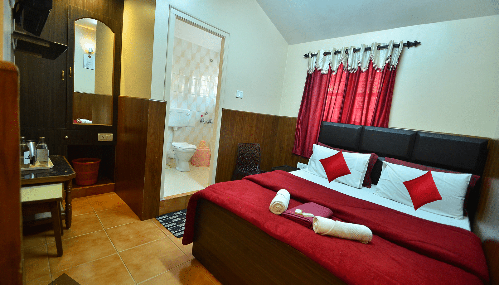Image of a room with a large bed and a washroom in the corner at BN Tourist Home, Ooty.