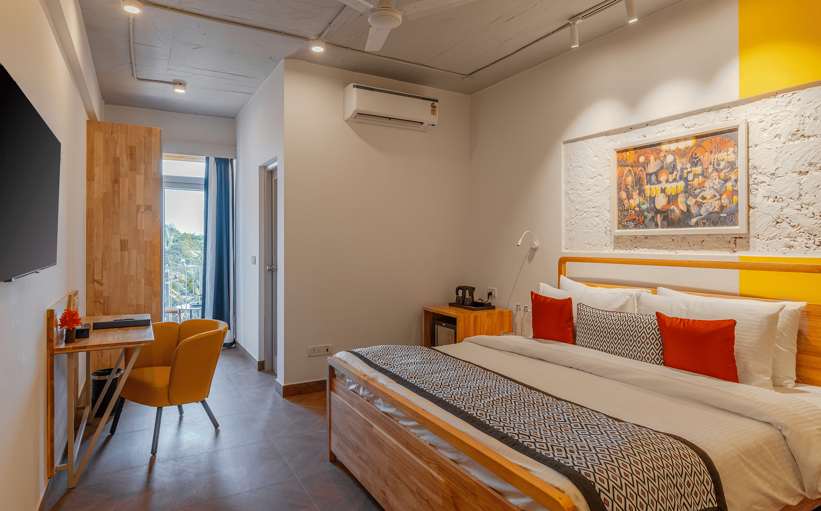 Bright hotel room with, flat TV screen, work desk and chair, vibrant art on the wall, and an access to the balcony at Bedzzz Xclusiv Morjim, Goa