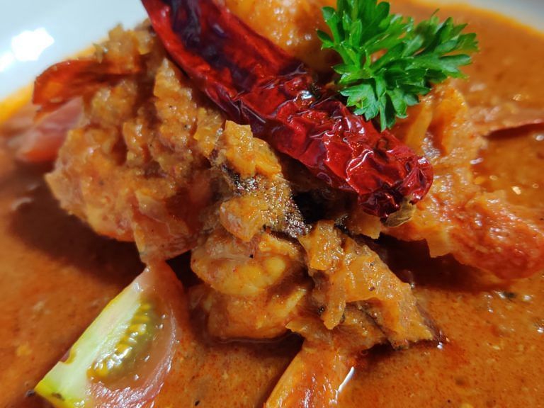 Dish of spicy chicken curry garnished with a red chilli and herbs.