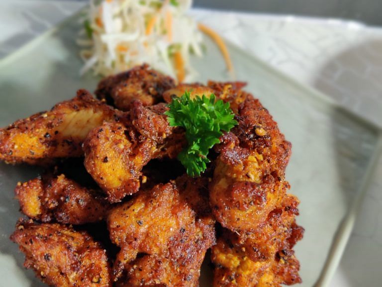 Plate of crispy fried chicken served with a side of fresh greens.