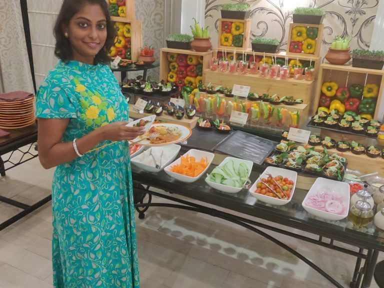 Woman standing near a buffet display of traditional dishes at an event.
