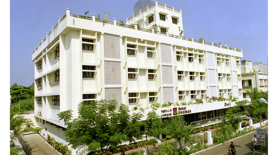 Daytime wide shot of the Hotel Pandian white multi-storey building facade surrounded by green trees - Hotel Pandian