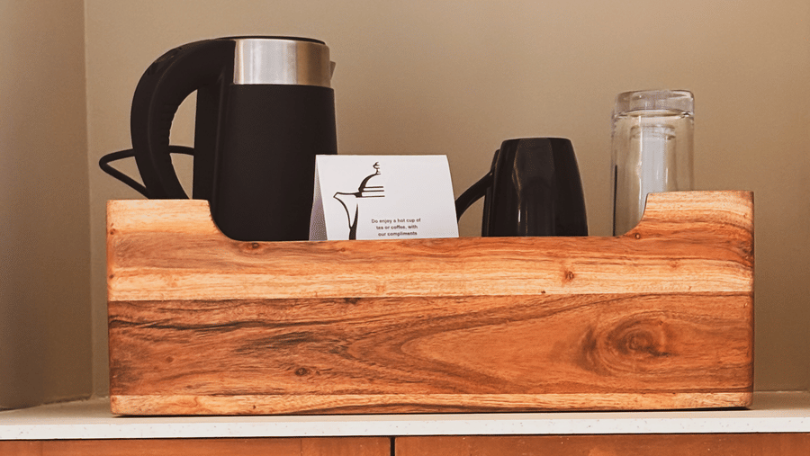 A black electric kettle and a white box are placed on a wooden tray atop a cabinet with mesh doors at Avanya Resorts N Retreat.