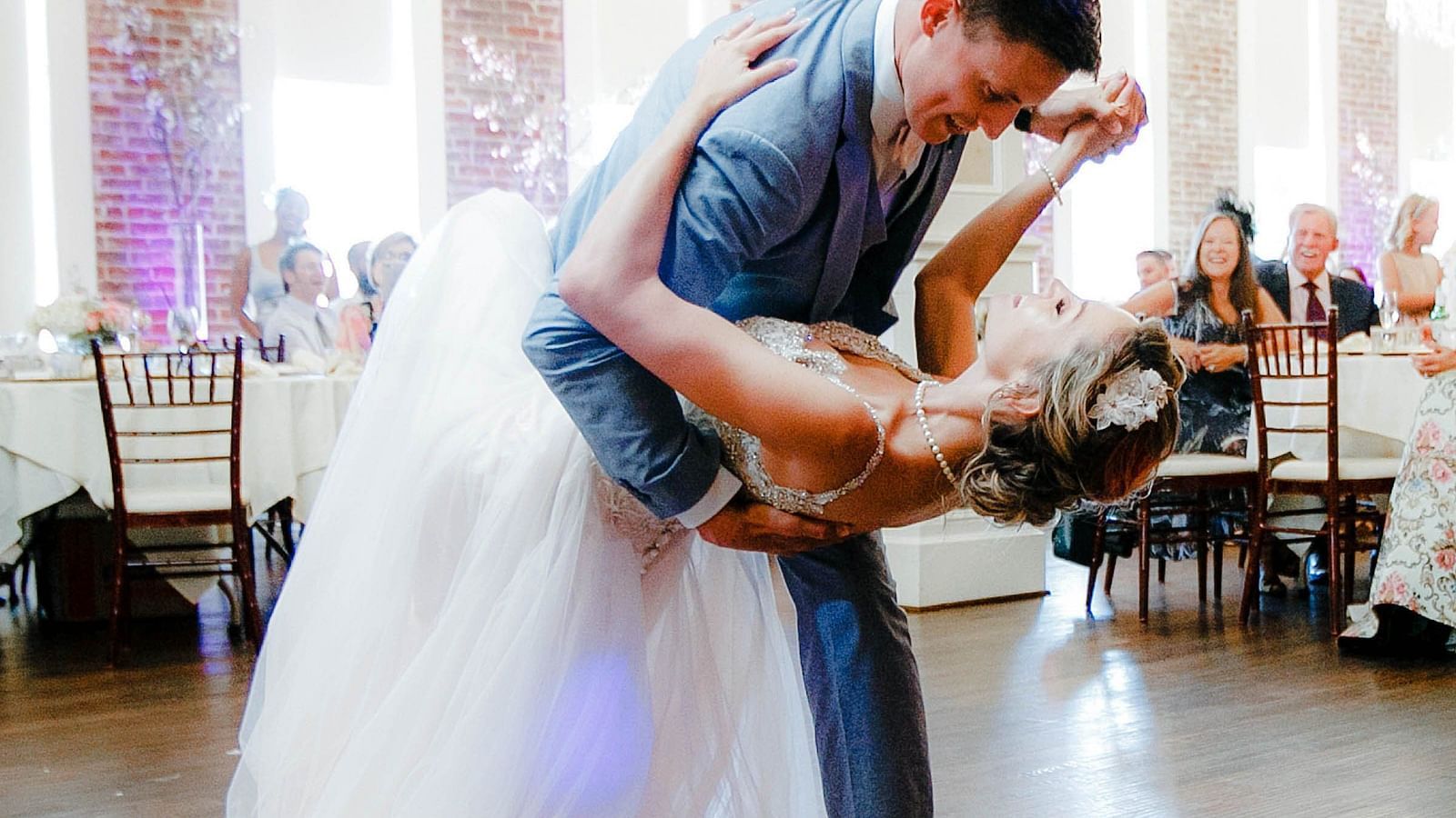 A bride and groom dancing during wedding celebration with people sitting behind the tables in the background. 